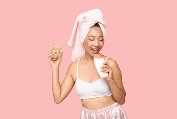 Young Asian woman with shower gel and loofah on pink background - obrazy, fototapety, plakaty