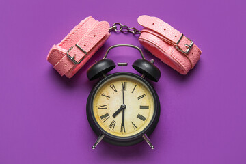 Alarm clock with handcuffs on purple background. Time for sex