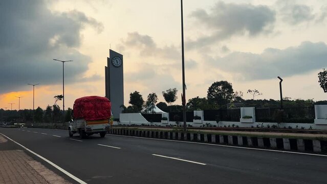 Monument with clock on Asian Avenue during sunset, shuttle passing by, India.