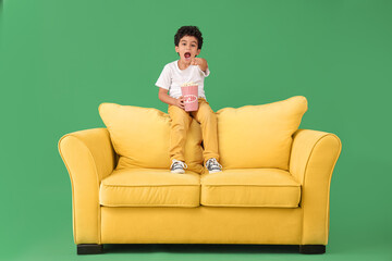 Little boy with popcorn on sofa pointing at viewer against green background