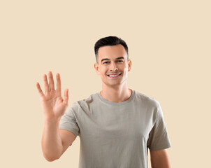 Young man waving hand on beige background