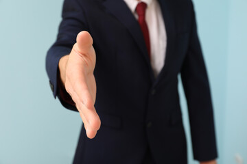 Businessman reaching out for handshake on blue background, closeup