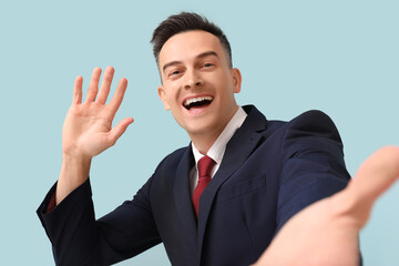 Handsome businessman waving hand on blue background, closeup