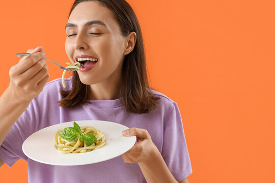 Young woman eating tasty pasta on orange background, closeup