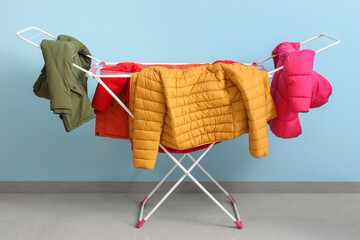 Clean puffer jackets hanging on dryer near blue wall © Pixel-Shot
