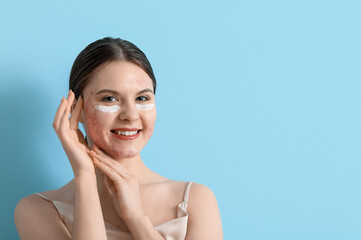 Young woman with acne problem and under-eye cream on blue background, closeup