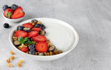 Yogurt bowl with granola and fresh berries: strawberries and blueberries on a gray background. 