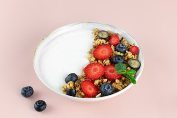 Yogurt bowl with granola and fresh berries: strawberries and blueberries on a pink background. 