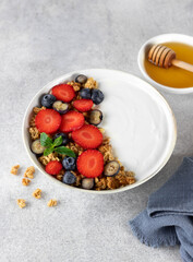 Yogurt bowl with granola and fresh berries: strawberries and blueberries on a gray background. Top view. 