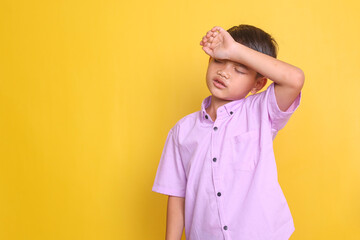 Young Asian little boy touching forehead feeling sickness and headache over yellow background