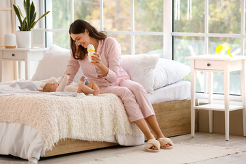 Mother with bottle of milk and her baby in bedroom