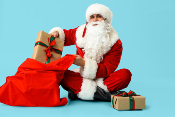 Santa Claus with bag and gift boxes sitting on blue background