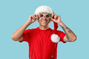 Young man in Santa hat with Christmas glasses on blue background