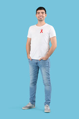 Fototapeta premium Handsome young man with red ribbon on blue background. World AIDS day concept