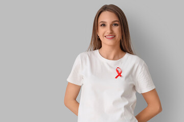 Obraz premium Pretty young woman with red ribbon on grey background. World AIDS day concept