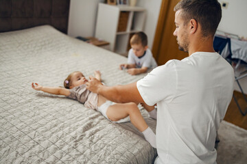 A father changing diaper while little girl is lying on the bed.
