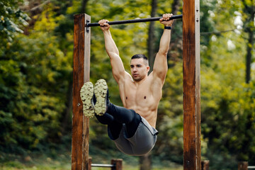 A shirtless sportsman is doing workouts in nature on pull up bar.