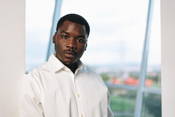 Young african man in white shirt and glasses posing near large window