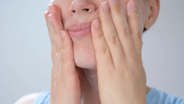 Young woman applying cleansing foam to her face close-up on a gray background.