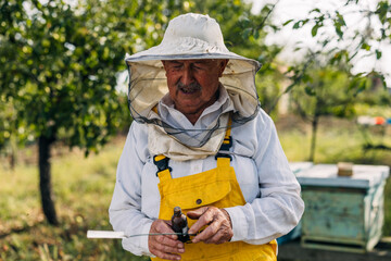 Front view of an old apiarist holding a bottle of propolis.