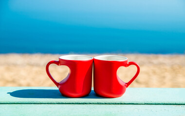 two heart shaped mugs with tea on the seashore
