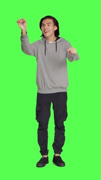 Front view of asian man acting as choir director for musical show, moving hands like a choirmaster chief over greenscreen backdrop. Male person conducting band to sing, smiling choirmaster musician.