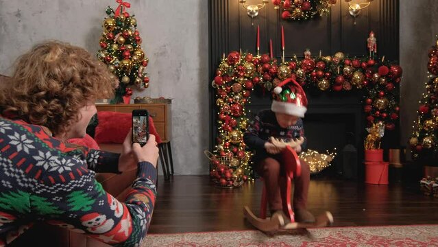 A Young Father Takes Pictures On The Smart Phone As His Son Plays In The Christmas Location
