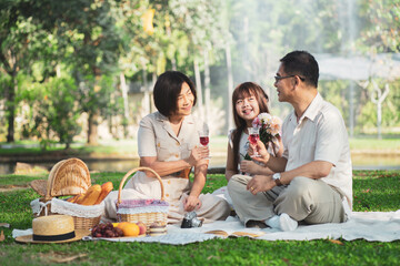 Happy Asian family enjoying picnic outing in the summer outdoors at the park.
