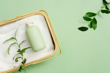 Rattan basket holds towels and unlabeled shower gel bottles on a pastel green background. Green tea...