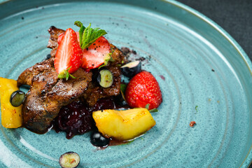 Baked goose liver with caramelized apple and strawberries. On a black stone background. In a plate,...