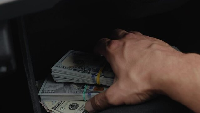 Close up a male pulling out a concealed handgun and a large sum of money from a car glove box compartment