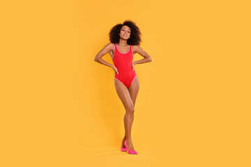 Beautiful woman in bright one-piece summer swimsuit and stylish high heel shoes on yellow background - obrazy, fototapety, plakaty