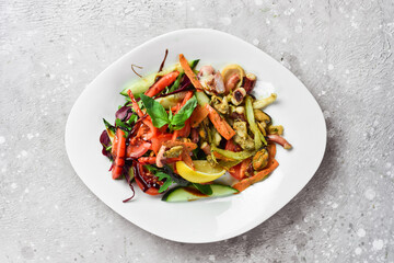 Vegetable salad with seafood. On a white plate. On a gray stone background. Restaurant menu.