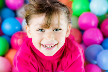 Fototapeta na wymiar Portrait of a cute happy little girl playing in a colorful plastic ball park 