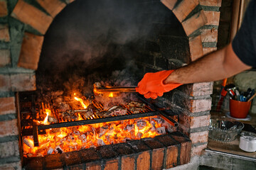 Cook in a mitten turns grilled ribs in a brick oven with tongs