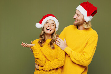 Merry young laughing smiling fun couple two friend man woman wear sweater Santa hat posing hug cuddle embrace isolated on plain green background. Happy New Year celebration Christmas holiday concept.