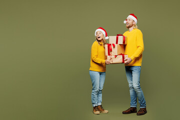 Full body merry young couple two friend man woman wear sweater Santa hat posing hold present boxes...