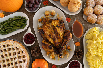 Thanksgiving day dinner table with roasted chicken or turkey, mashed potatoes, cranberry sauce, gravy, apple pie and other holiday season foods. Traditional autumn fall feast flat lay composition.