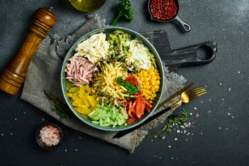 A plate of colorful vegetable salad made of cucumber, paprika, tomatoes, potatoes and boiled sausage. On a dark stone background.