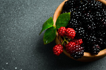 A wooden bowl with berries. Fresh blackberry berries and green leaves close-up, top view.
