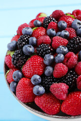 Different fresh ripe berries in bowl on light blue table, closeup