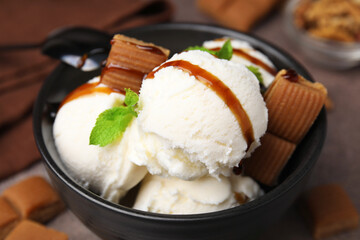 Bowl of tasty ice cream with caramel sauce, candies and mint on table, closeup