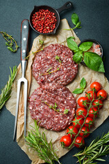 Raw veal burger cutlet with spices and herbs. Ready to cook. On a dark stone background. Top view.