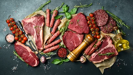 Fotobehang Set of meat and meat products. T-bone steak, ribeye steak, kebab and burger patty. On a black stone background. Top view. © Yaruniv-Studio