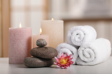 Spa composition. Burning candles, lotus flower, stones and towels on white table