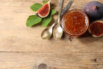 Glass jar with tasty sweet jam, spoons and fresh figs on wooden table, flat lay. Space for text