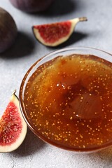 Glass bowl of tasty sweet jam and fresh figs on light table, closeup