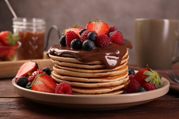 Stack of tasty pancakes with fresh berries and chocolate spread on wooden table, closeup