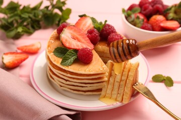 Dripping honey onto delicious pancakes with fresh berries on pink table, closeup