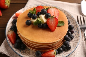 Delicious pancakes with fresh berries and butter served on wooden table, closeup